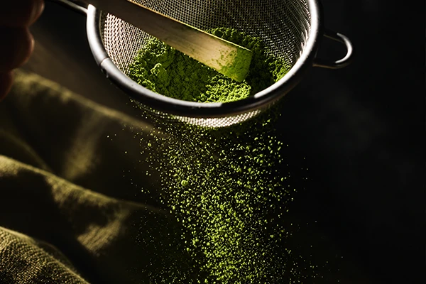 Fine matcha powder being sifted through a metal sieve.