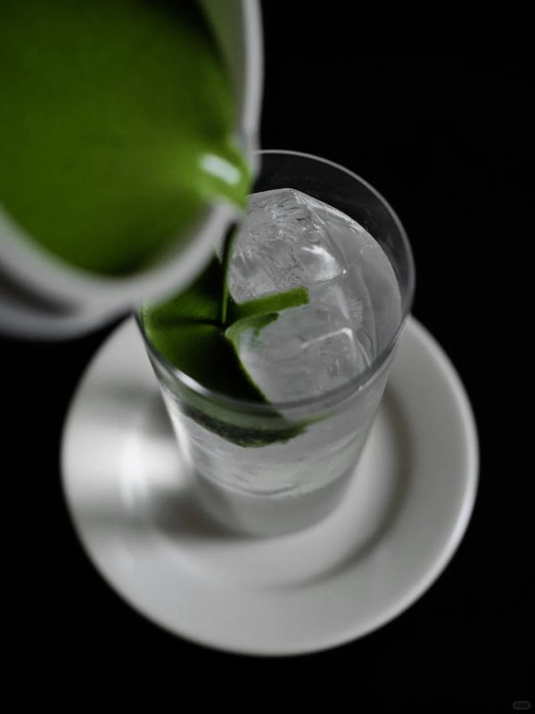 Matcha coconut water refresher being poured over ice in a tall glass.