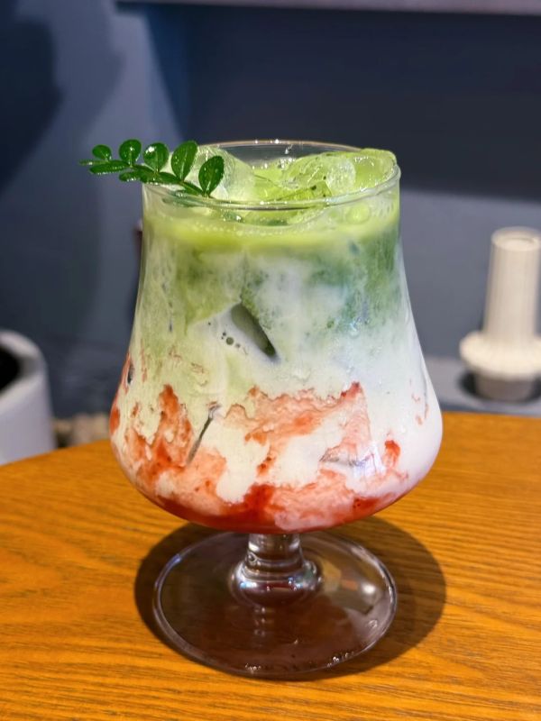 Layered matcha strawberry milk in a goblet glass with strawberry streaks and iced matcha on top