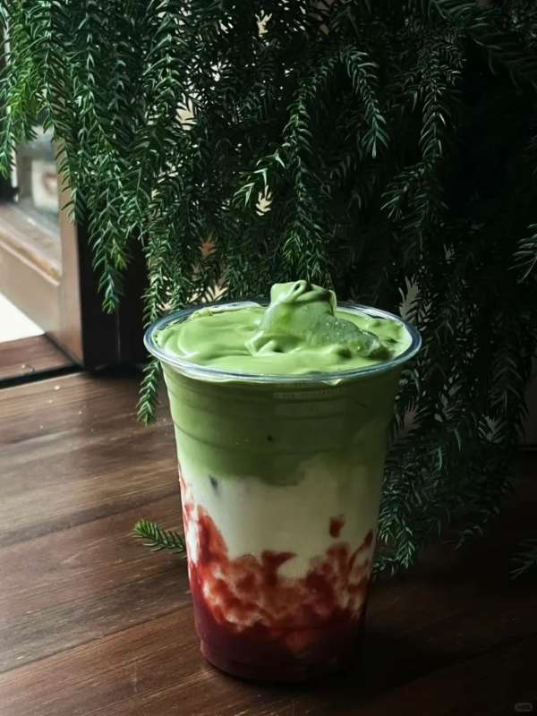 Iced matcha strawberry milk in a tall plastic cup with strawberry, milk and matcha layers.