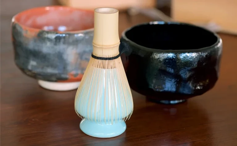 Bamboo matcha whisk resting on a ceramic whisk stand, or kusenaoshi.