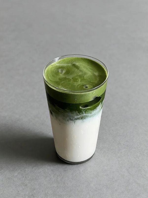Thick coconut matcha latte in a tall glass with green matcha over white coconut milk.